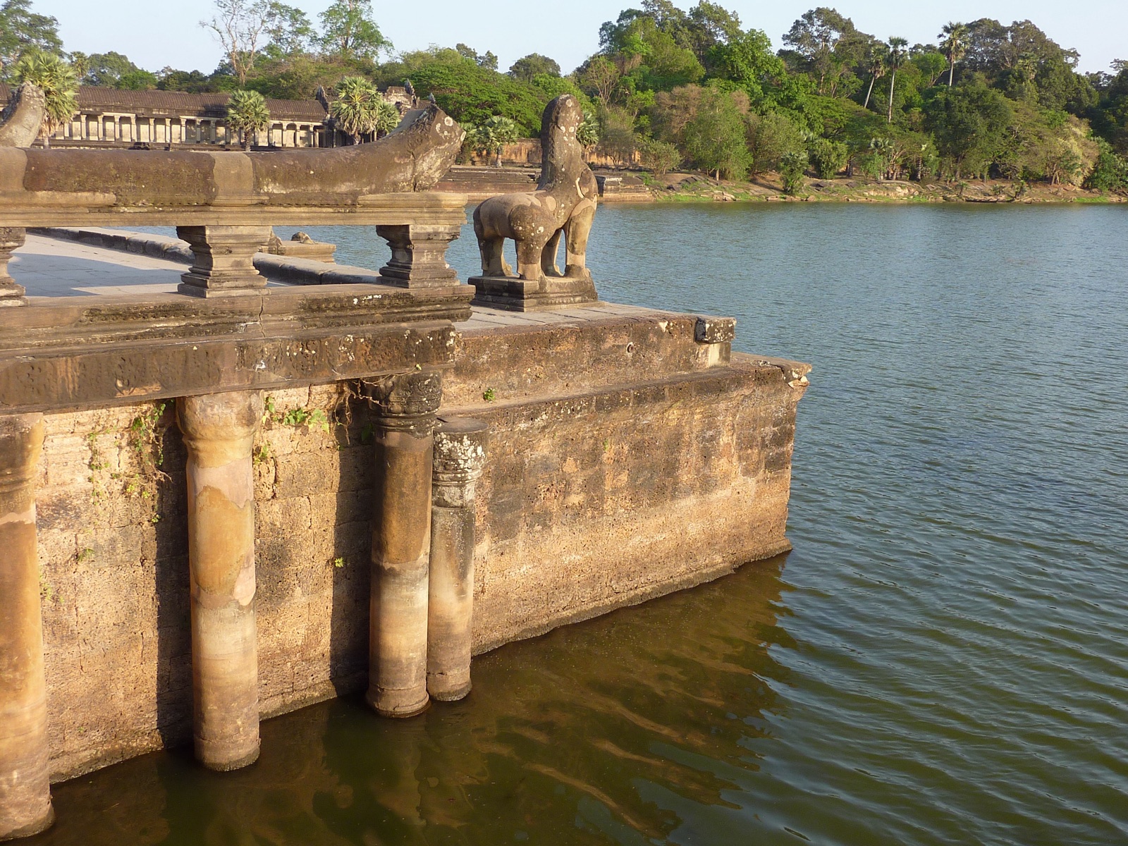 A corner of Angkor Wat's moat and western causeway, with a carved lion guardian and the outer gallery visible across the water. Photo: Photo Dharma, CC BY 2.0, via Wikimedia Commons.